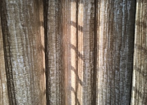 Vertical, textured curtains with light streaming through, creating a pattern of shadows.