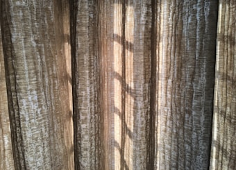 Vertical, textured curtains with light streaming through, creating a pattern of shadows.