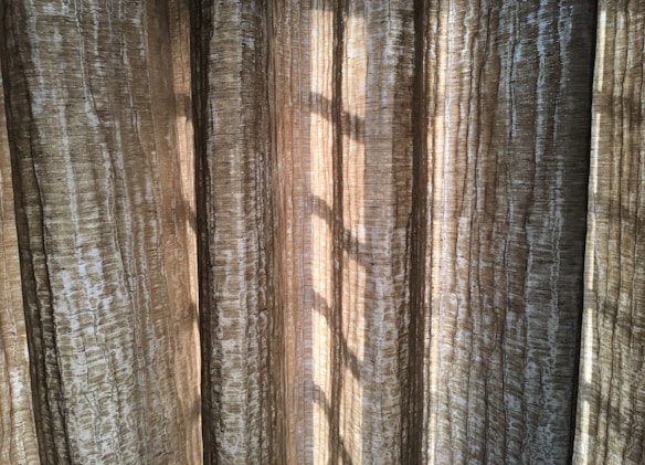 Vertical, textured curtains with light streaming through, creating a pattern of shadows.