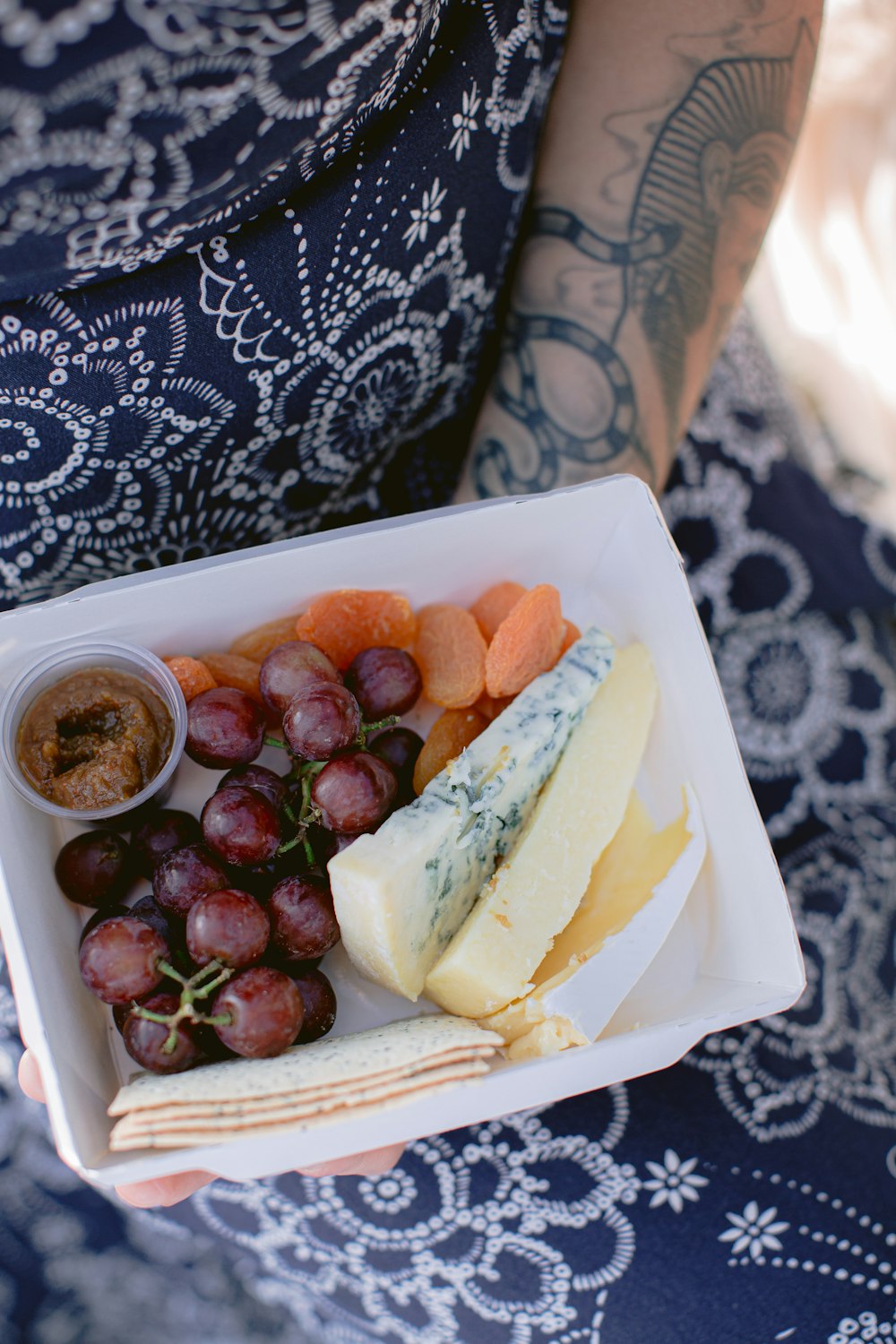 a person holding a plate of food with grapes and cheese