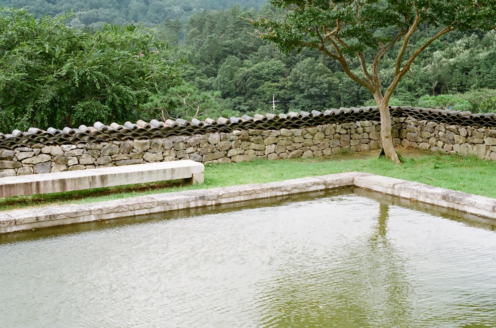 a stone wall next to a small pond