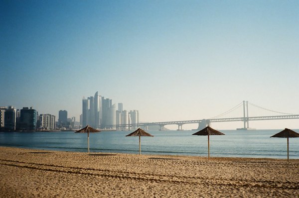 A beach with umbrellas and a bridge in the background — Busan, South Korea