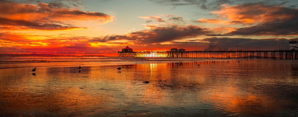 a sunset at a beach with a pier in the background
