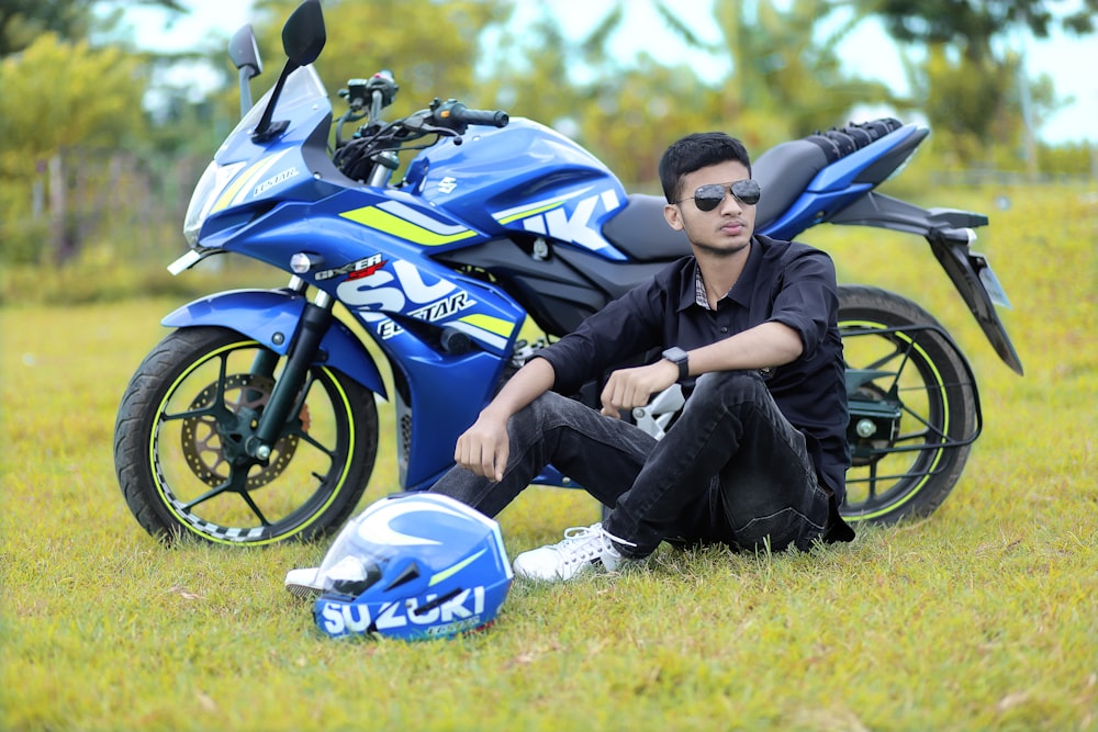 a man sitting on the ground next to a blue motorcycle
