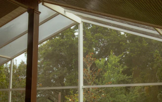 Sunlit veranda with crystal-clear glass panels and lush greenery outside.