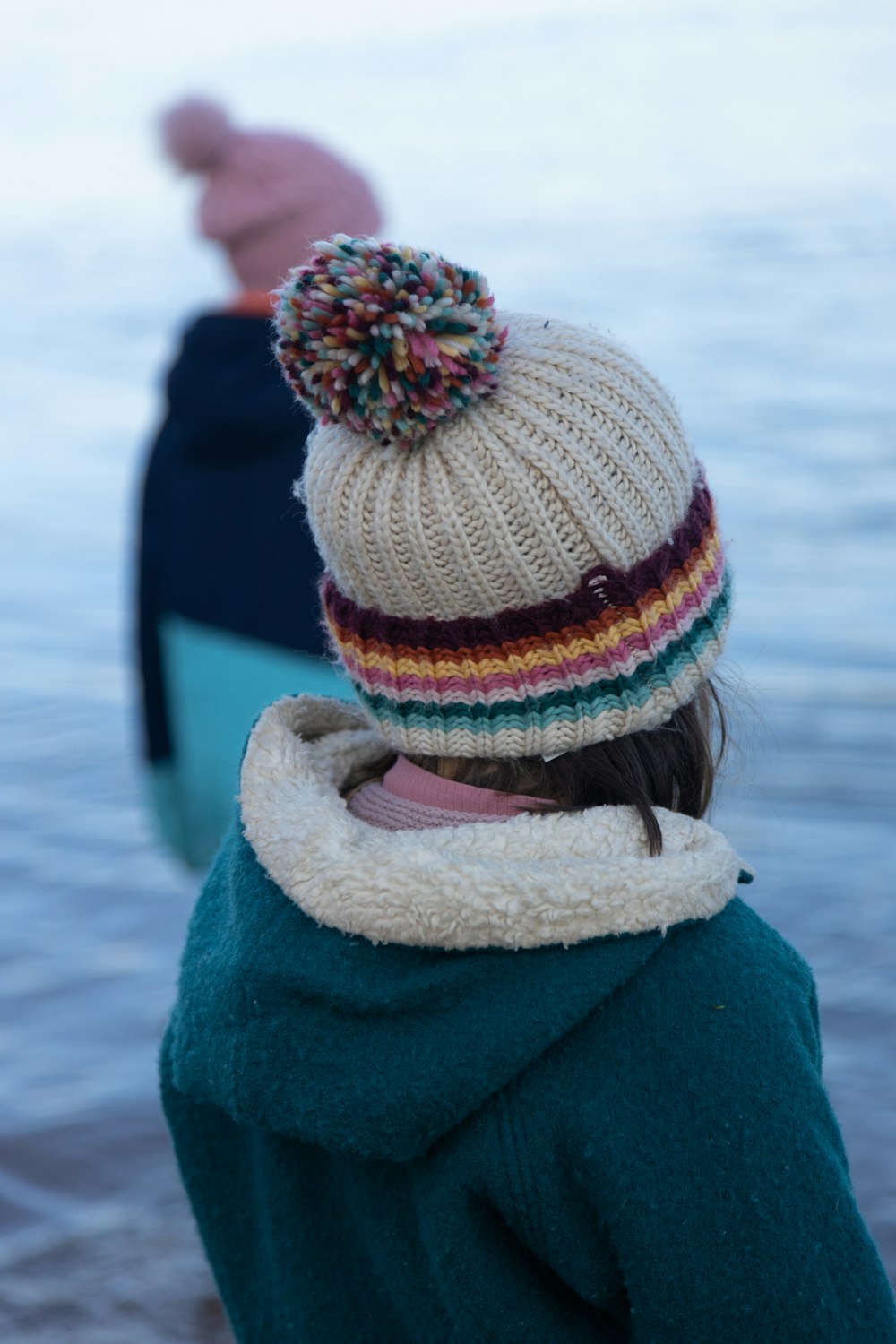 a person wearing a hat and a coat by a body of water
