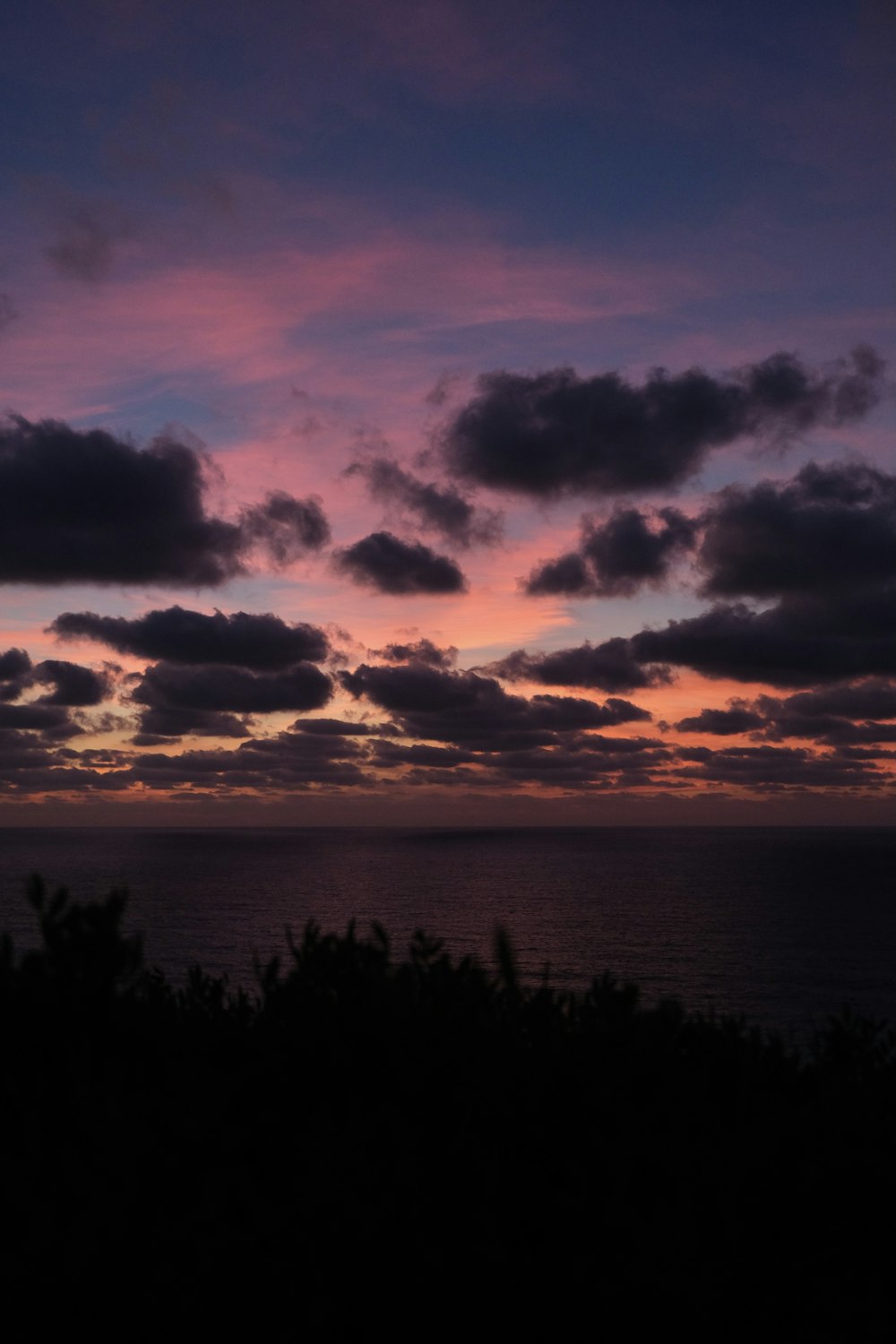 the sun is setting over the ocean with clouds in the sky