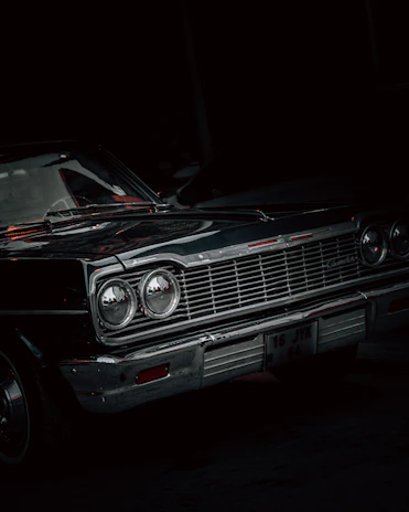 Classic car with a glossy black finish displayed against a minimalist urban backdrop at twilight.