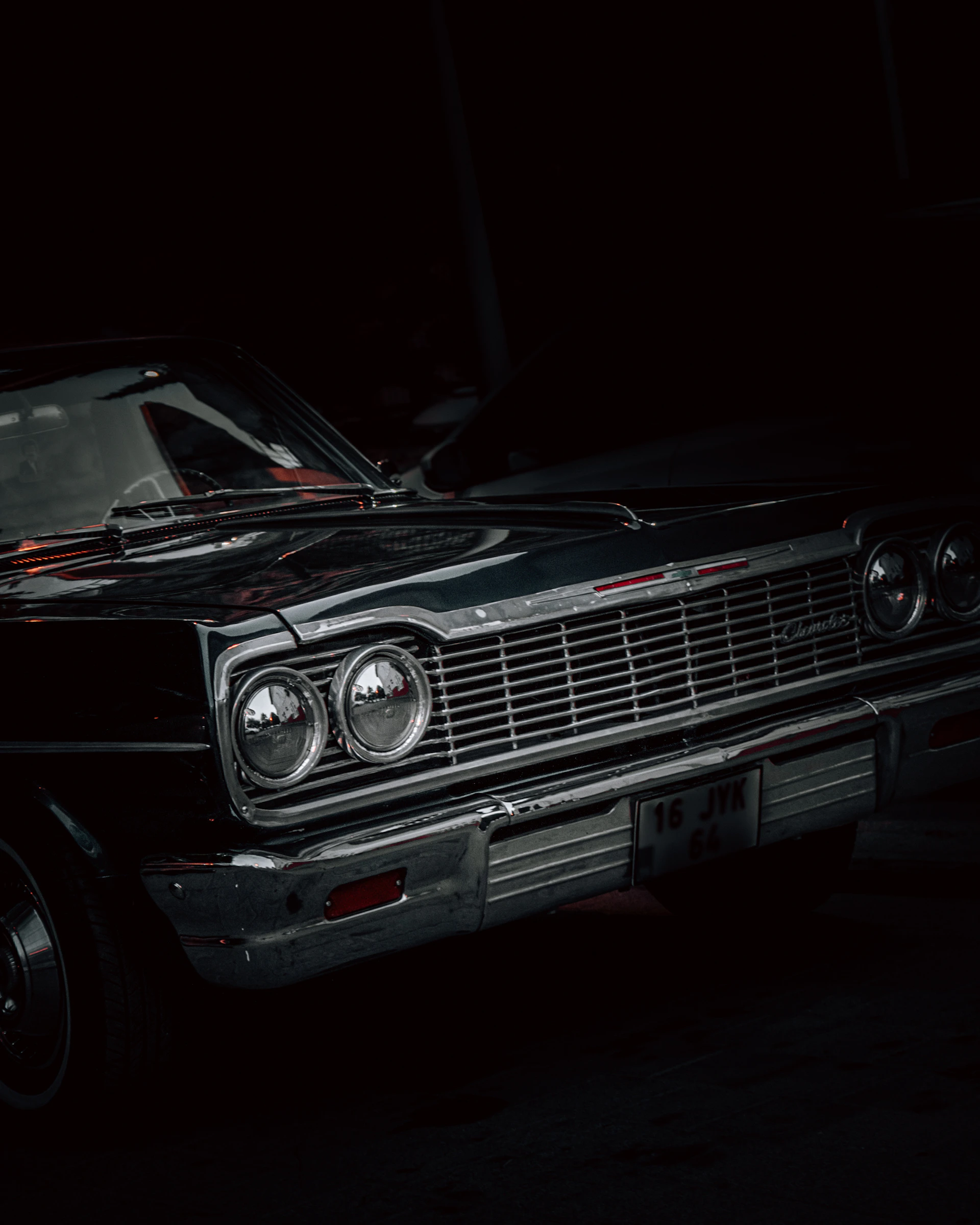 A close-up of a classic car parked beside the stage, its polished chrome reflecting the neon glow of the nightclub.