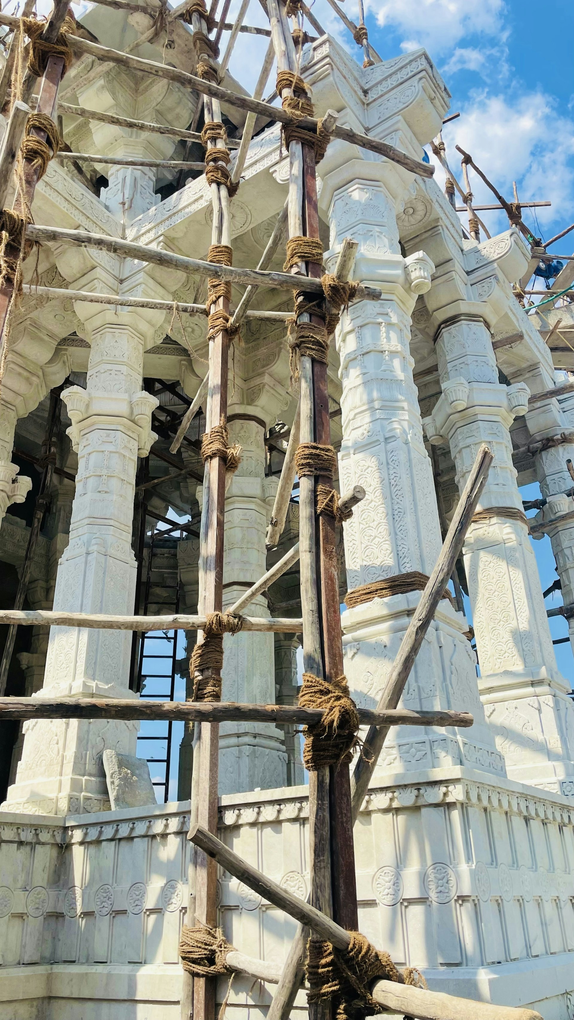A serene Jain temple under construction, with workers laying the foundation and precise stone arrangements.