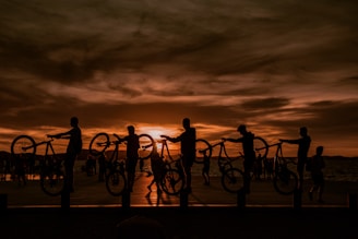 A sunset silhouette of a group of cyclists raising their bikes in celebration after a challenging ride.