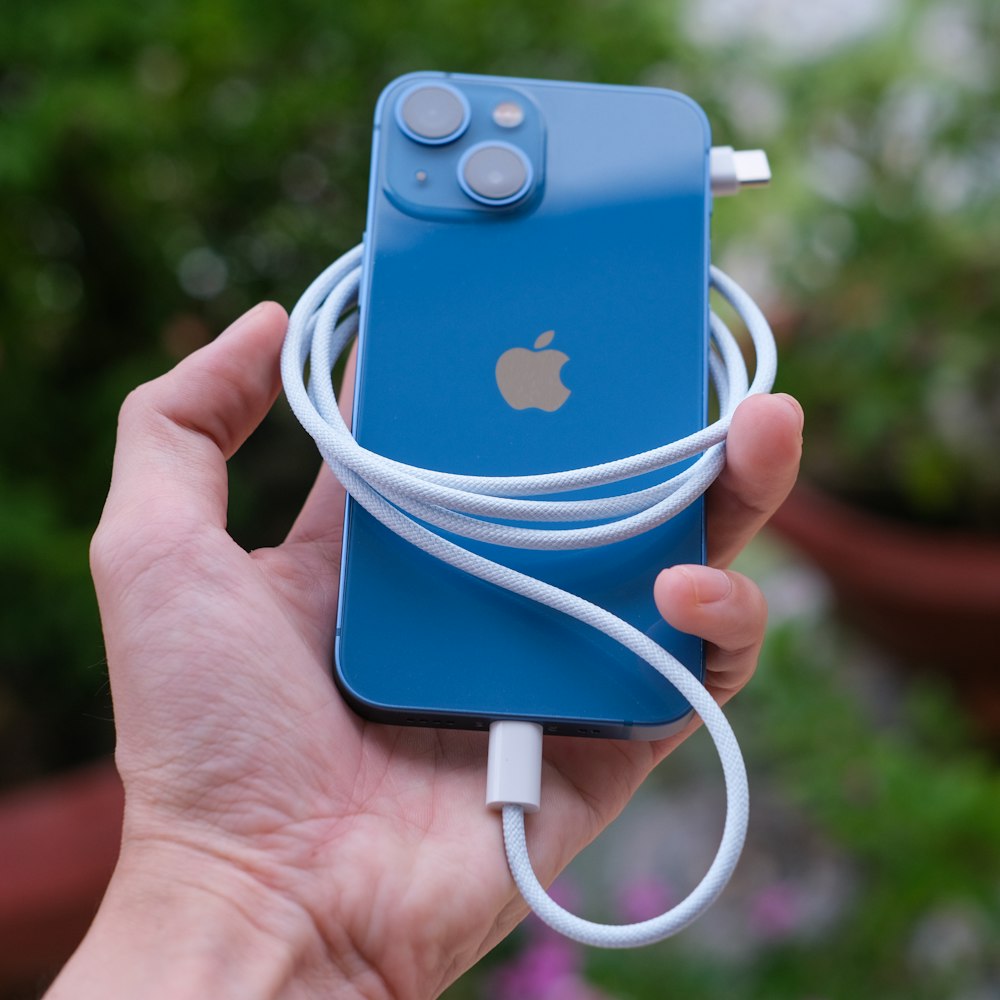 a hand holding a blue apple device with a white cord