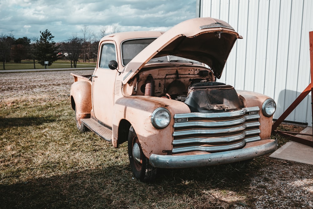 an old truck with its hood open sitting in the grass