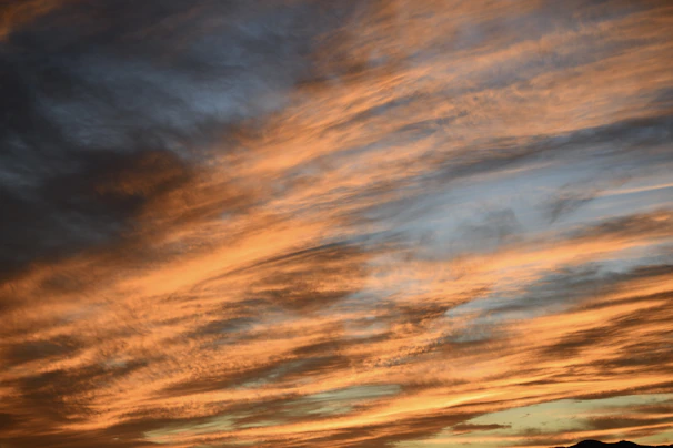 A vibrant sunset sky with streaks of orange and purple clouds over a calm horizon.