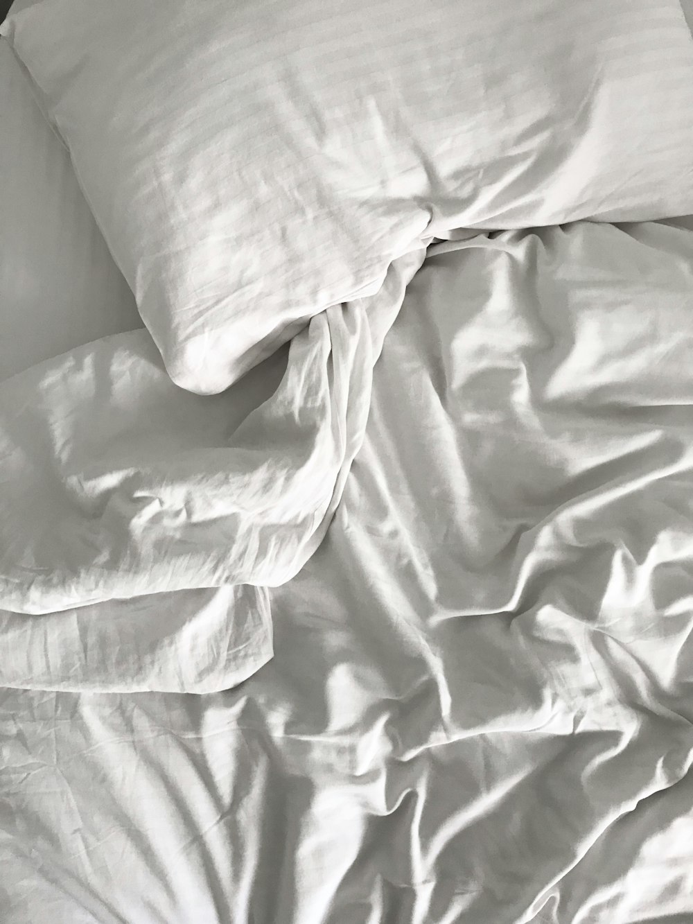 an unmade bed with white sheets and pillows