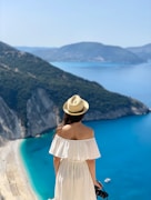 a woman in a white dress and hat looking at the ocean