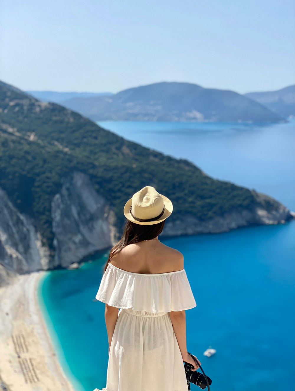 a woman in a white dress and hat looking at the ocean