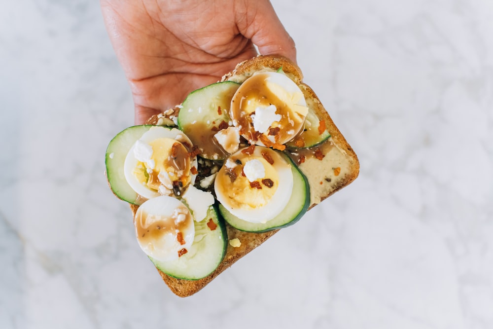 a person holding a piece of bread with sliced cucumbers on it