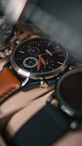 A close-up view of a sophisticated wristwatch with a black dial and a brown leather strap. The watch features intricate details, including multiple sub-dials and silver accents. The focus is on the craftsmanship and elegance of the timepiece.