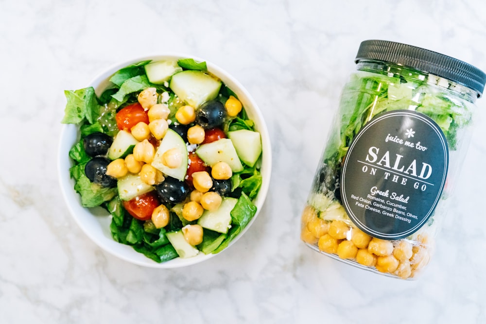 a salad in a bowl next to a jar of salad dressing