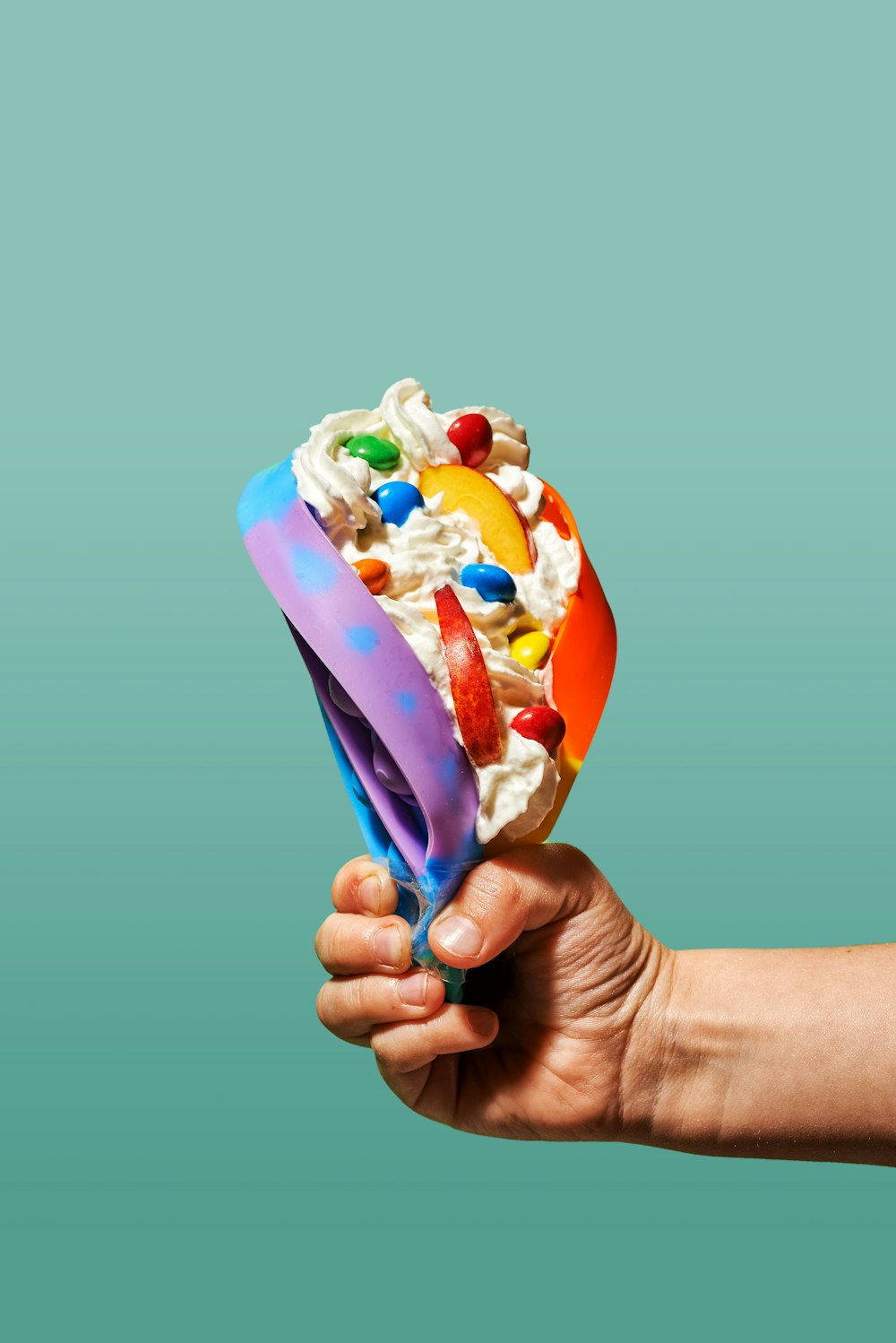 Una mano sosteniendo una bola de helado con ingredientes coloridos