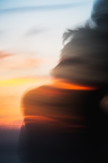 A warm, abstract image blending light sunny blue hues with a silhouette of a person watching a sunset.