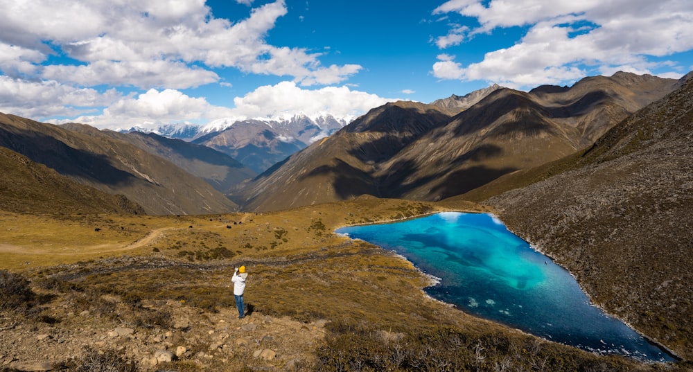 a man standing on top of a mountain next to a lake