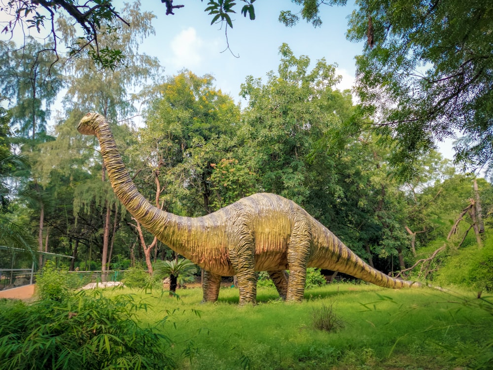 une statue d’un dinosaure dans une zone herbeuse