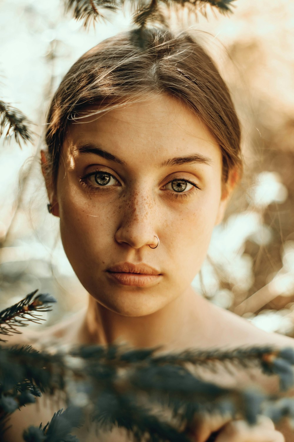 a woman with freckles on her face standing in front of a tree