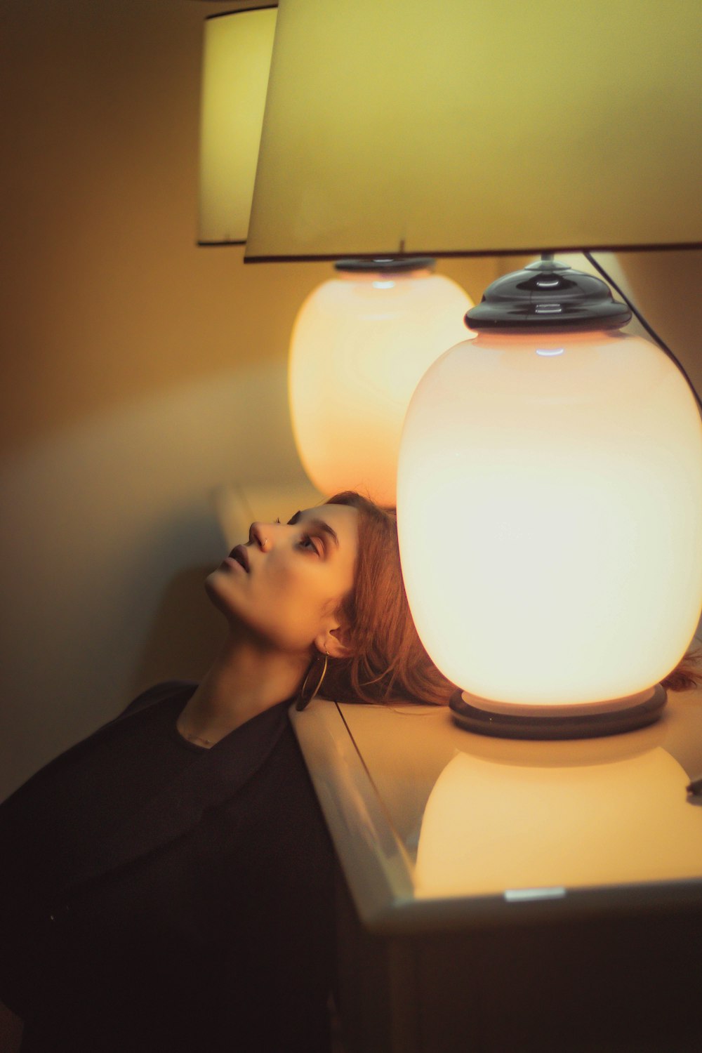 a woman standing next to a table with a lamp on top of it