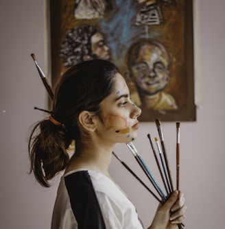 a woman holding a bunch of paint brushes