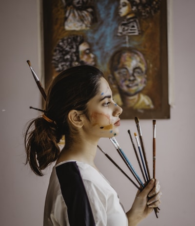 a woman holding a bunch of paint brushes