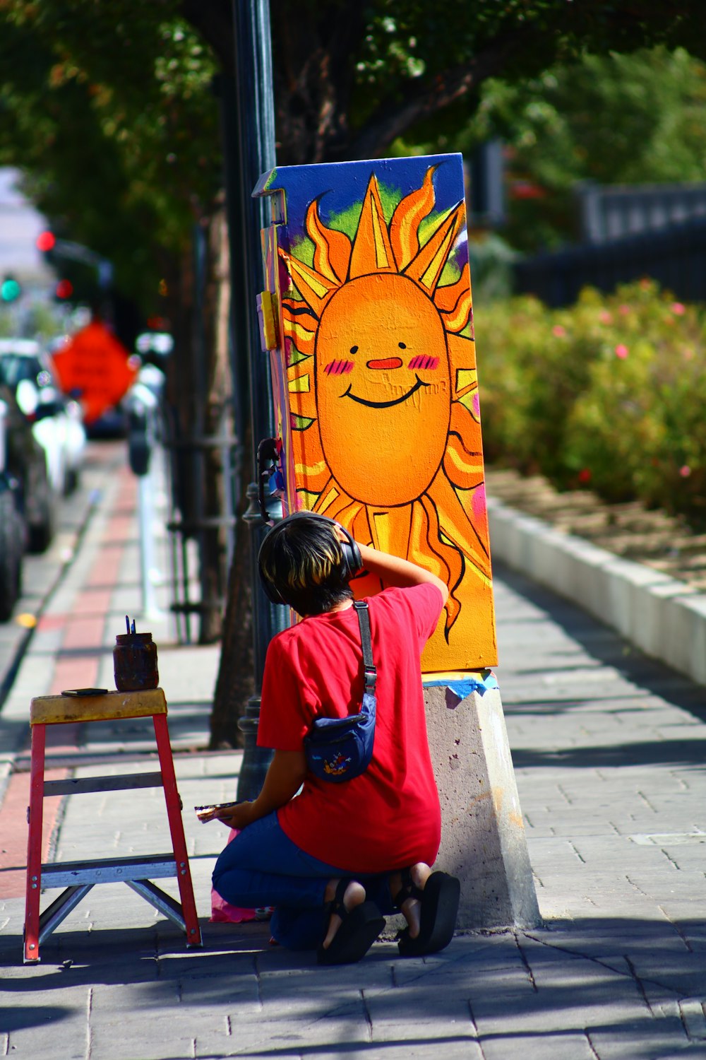 a woman sitting on a sidewalk next to a painting