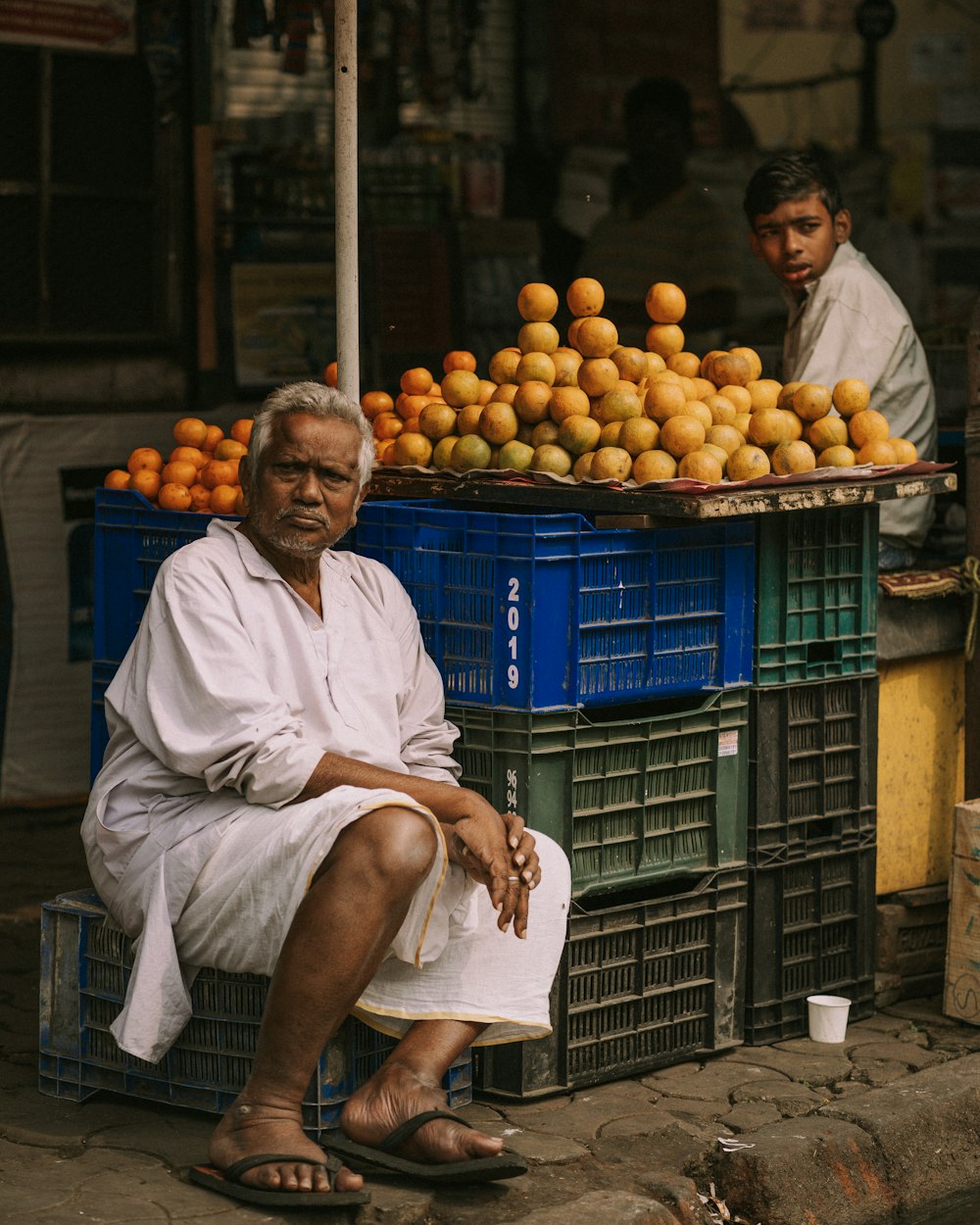 a man sitting in front of a pile of oranges