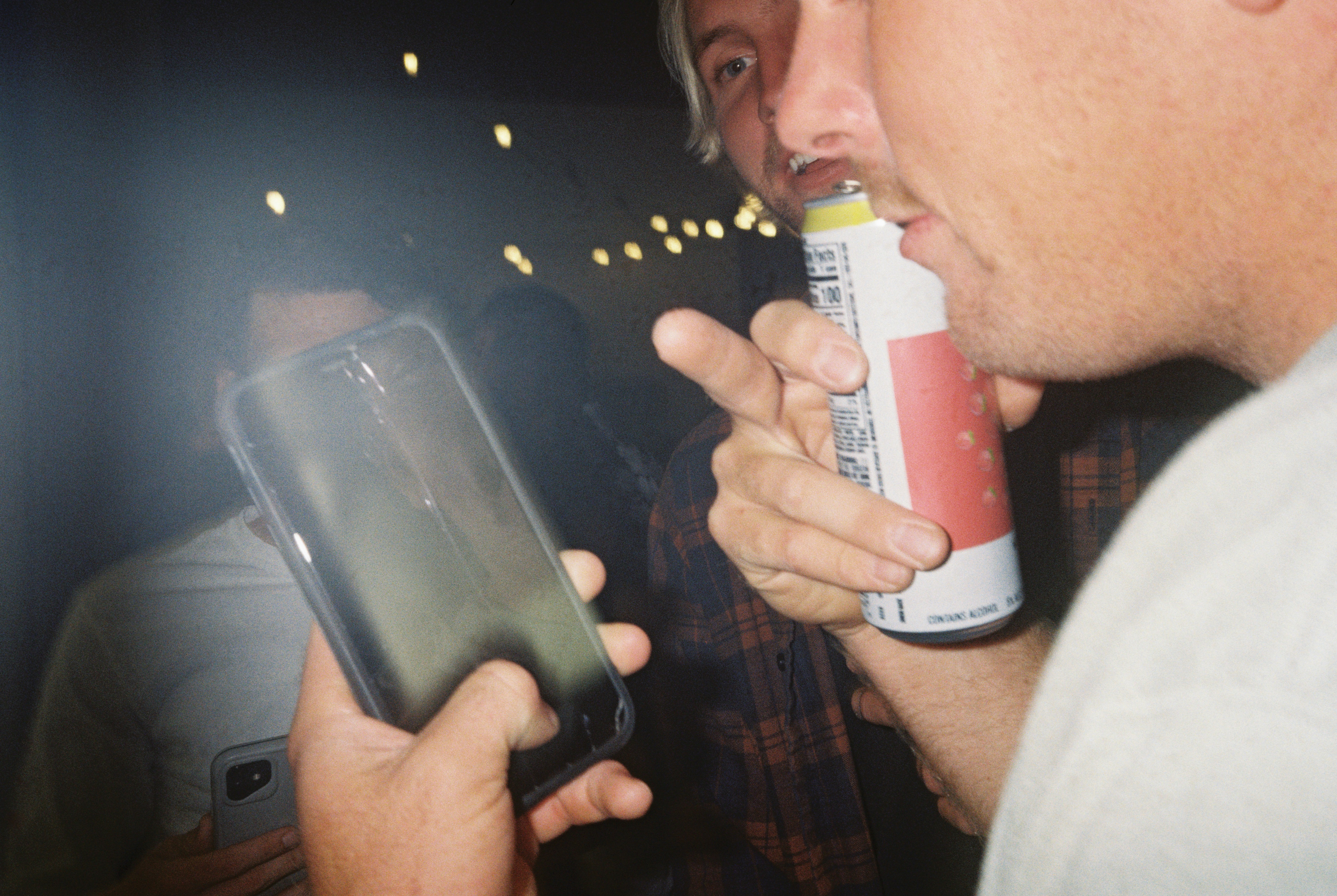a man holding a can of soda and a cell phone