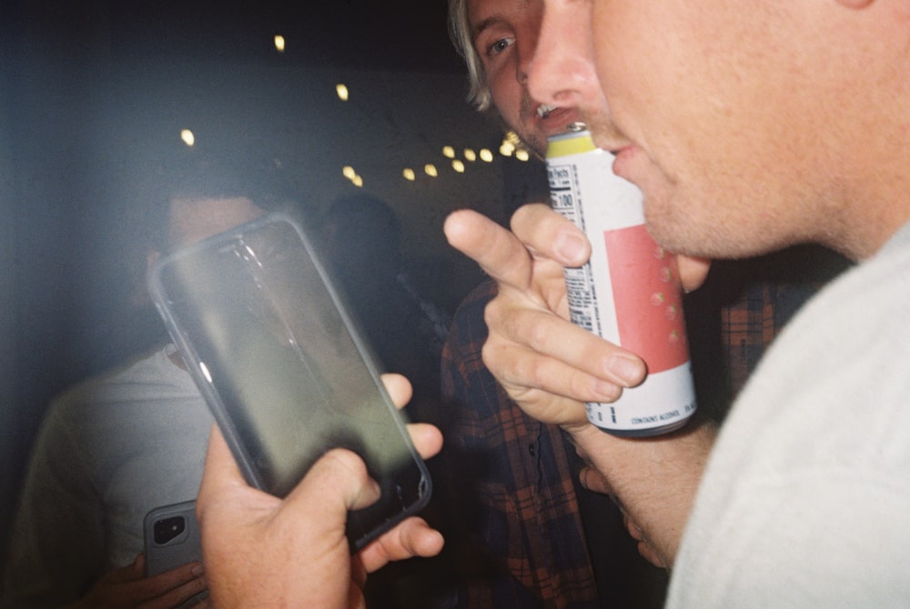 a man holding a can of soda and a cell phone