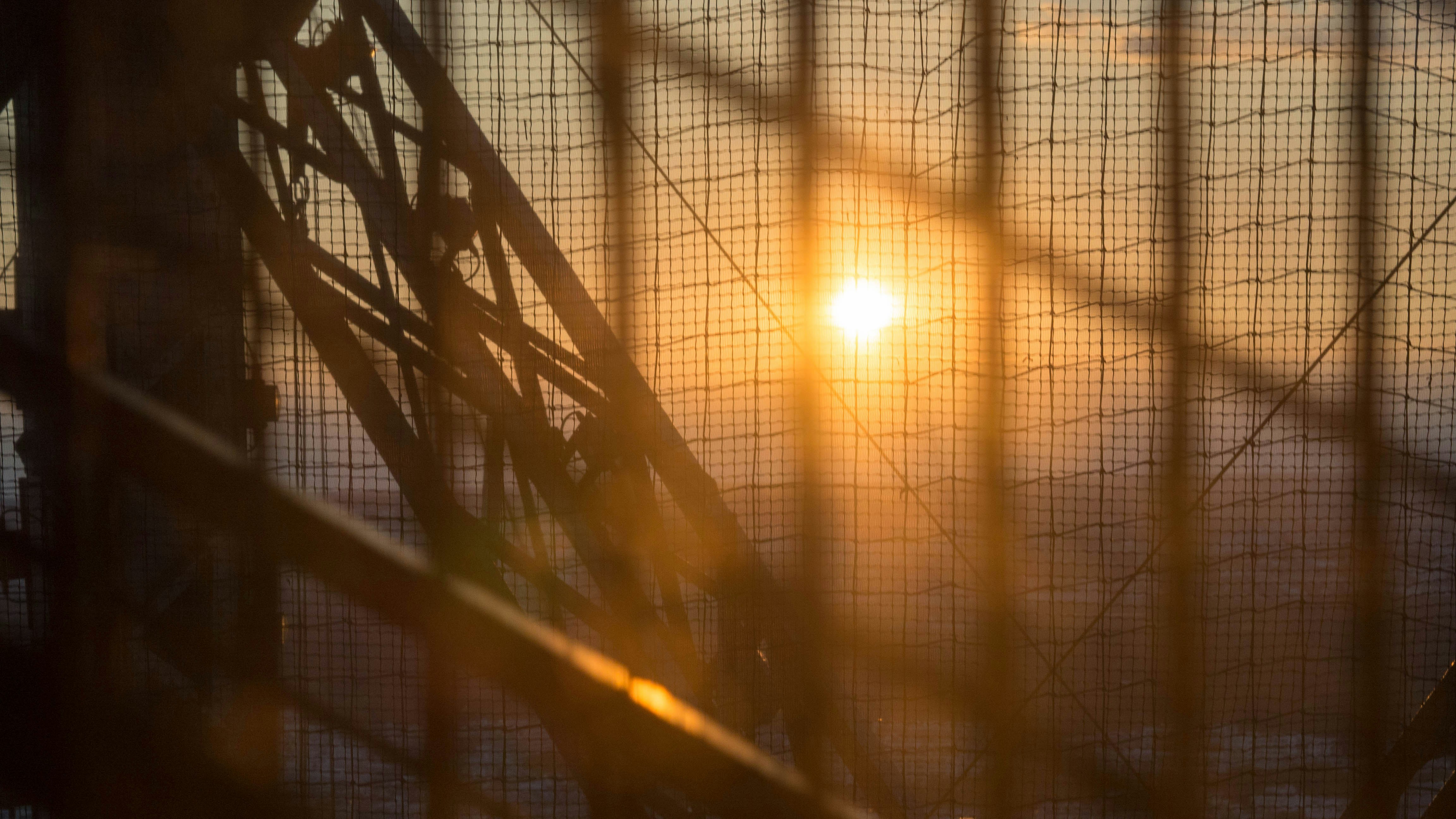 the sun is setting behind a wire fence