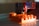 A close-up view of a 3D printer in operation with an orange object being printed. The printer nozzle is depositing filament, creating a layered structure. The surrounding area is slightly blurred, focusing attention on the printing process.