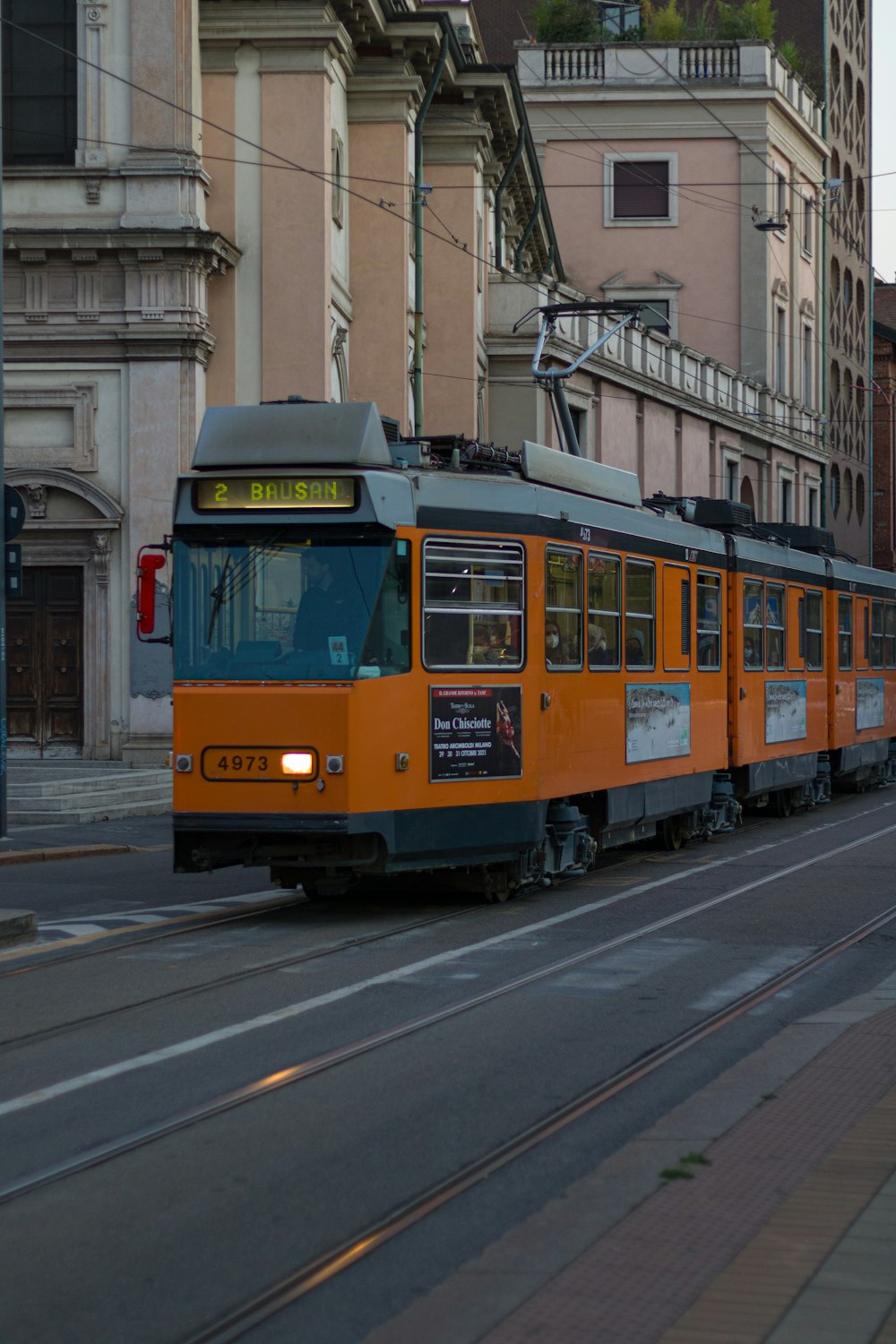 an orange train traveling down a street next to tall buildings