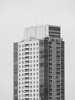A tall building with a modern design, featuring large windows and numerous balconies distributed evenly across its facade. The exterior combines sections of smooth surfaces with grid-like patterns.