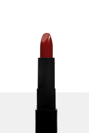 A tube of red lipstick stands upright against a plain white background. The lipstick is still intact, with a smooth surface and a glossy finish. The tube is black and sleek, providing a contrast against the vibrant red color of the lipstick.