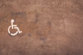 A textured brown surface features a white wheelchair accessibility symbol painted on it. The wall appears to have a rough, weathered texture with visible brush strokes.