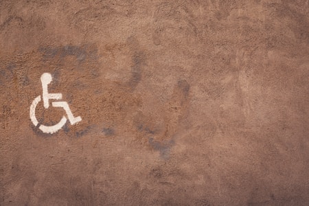 A textured brown surface features a white wheelchair accessibility symbol painted on it. The wall appears to have a rough, weathered texture with visible brush strokes.