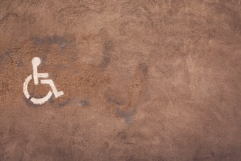 A textured brown surface features a white wheelchair accessibility symbol painted on it. The wall appears to have a rough, weathered texture with visible brush strokes.