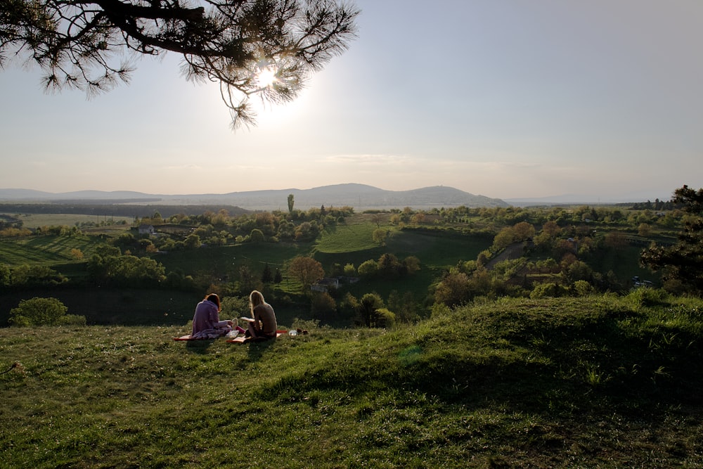 a couple of people sitting on top of a lush green hillside