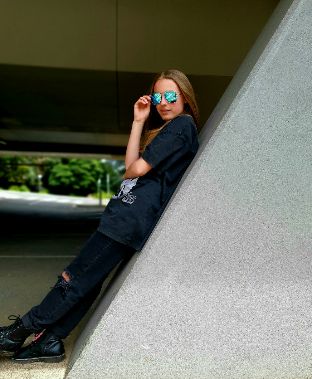 a girl wearing sunglasses leaning against a wall