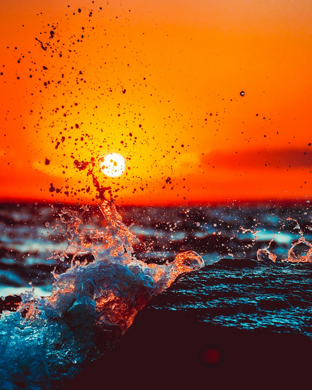 the sun is setting over the ocean with a splash of water