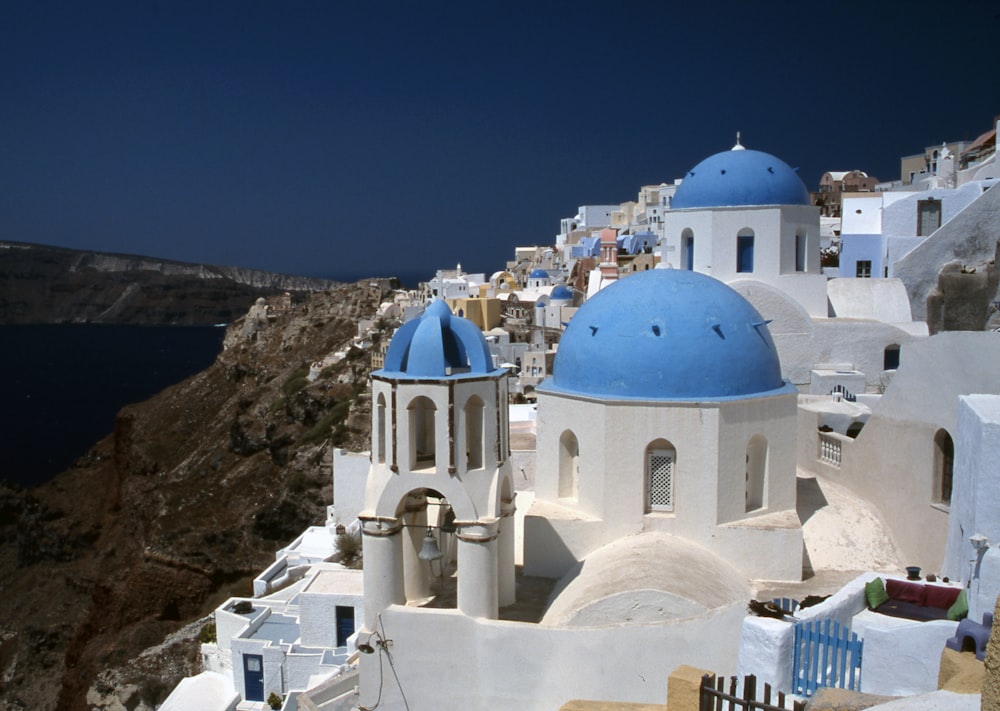 a blue and white church on a cliff overlooking a body of water