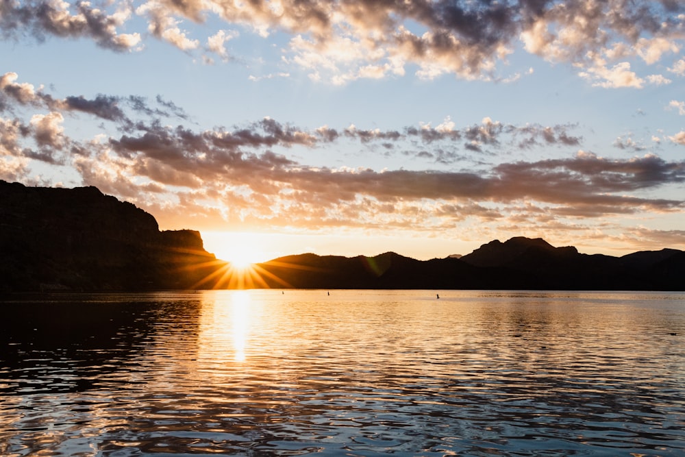 the sun is setting over a lake with mountains in the background