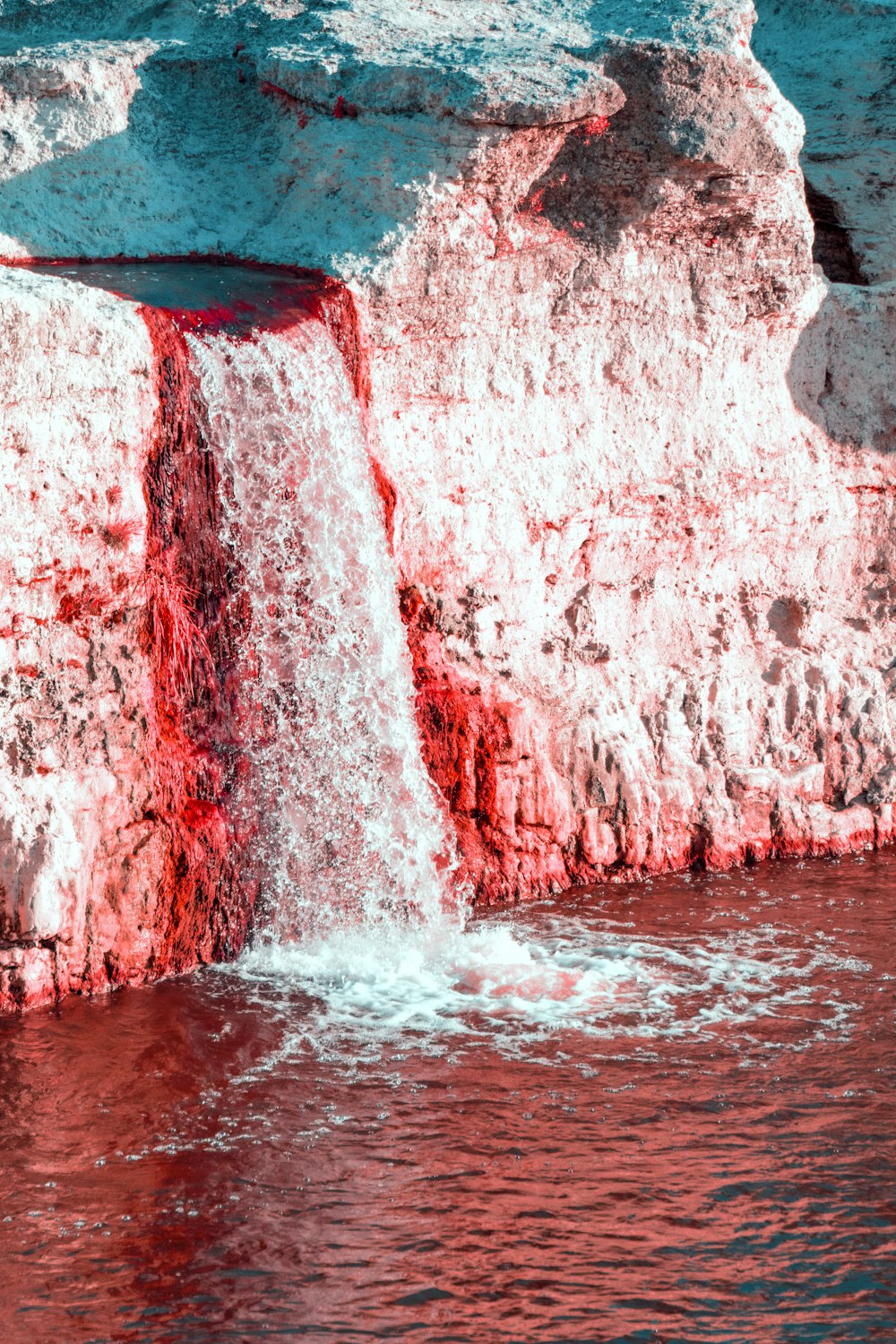 a red and white waterfall in the middle of a body of water